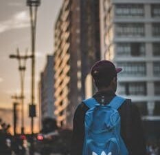 A man with a blue backpack walks through the city at sunset, embracing the urban landscape.